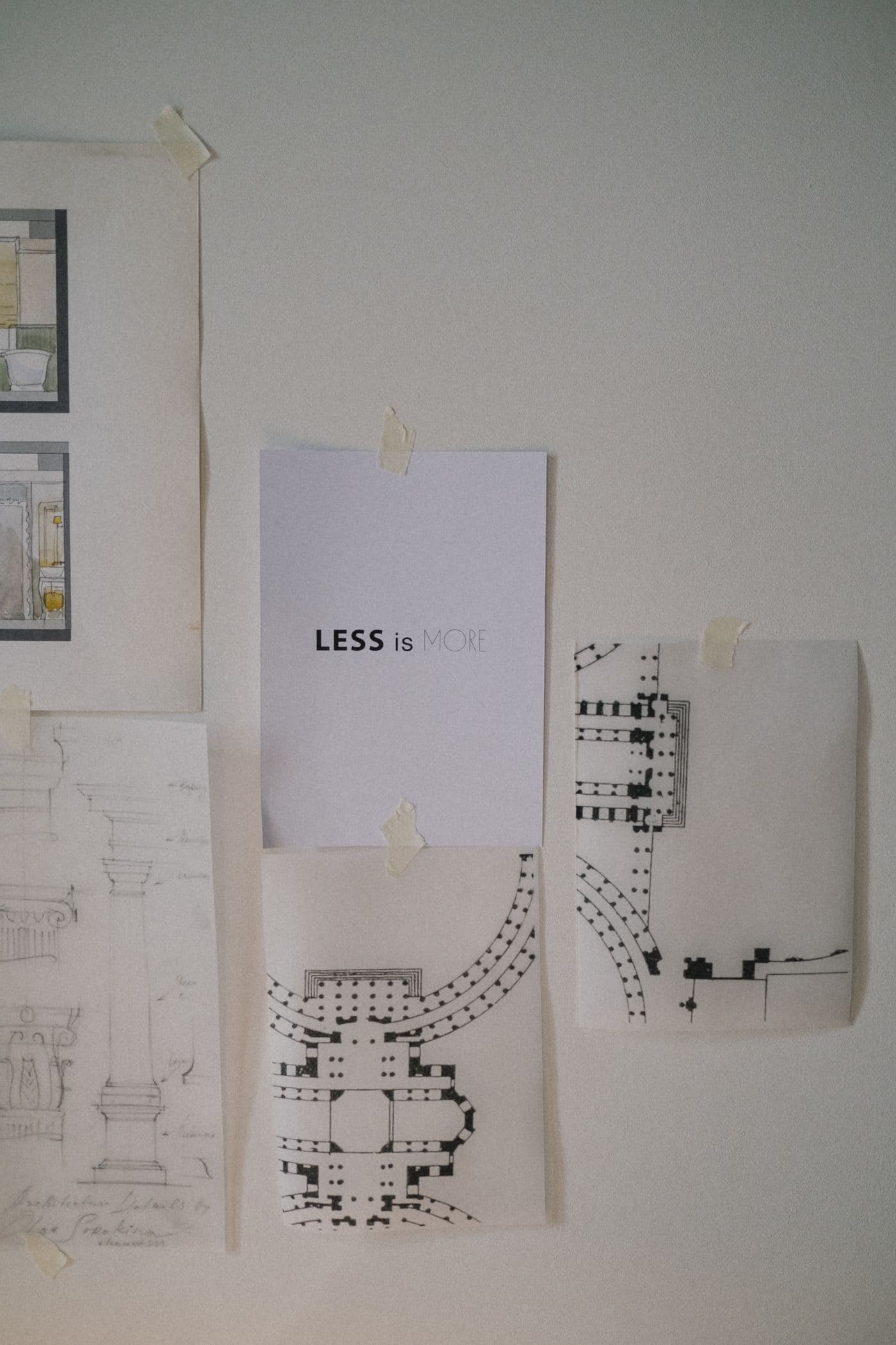 Drafts and sketches taped to a plain studio wall in neutral light