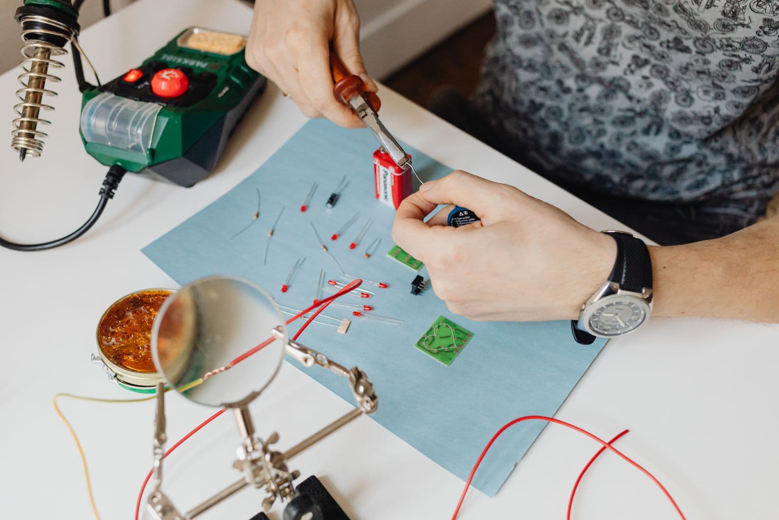 Two hands trimming component leads with pliers over a breadboard at a soldering station.