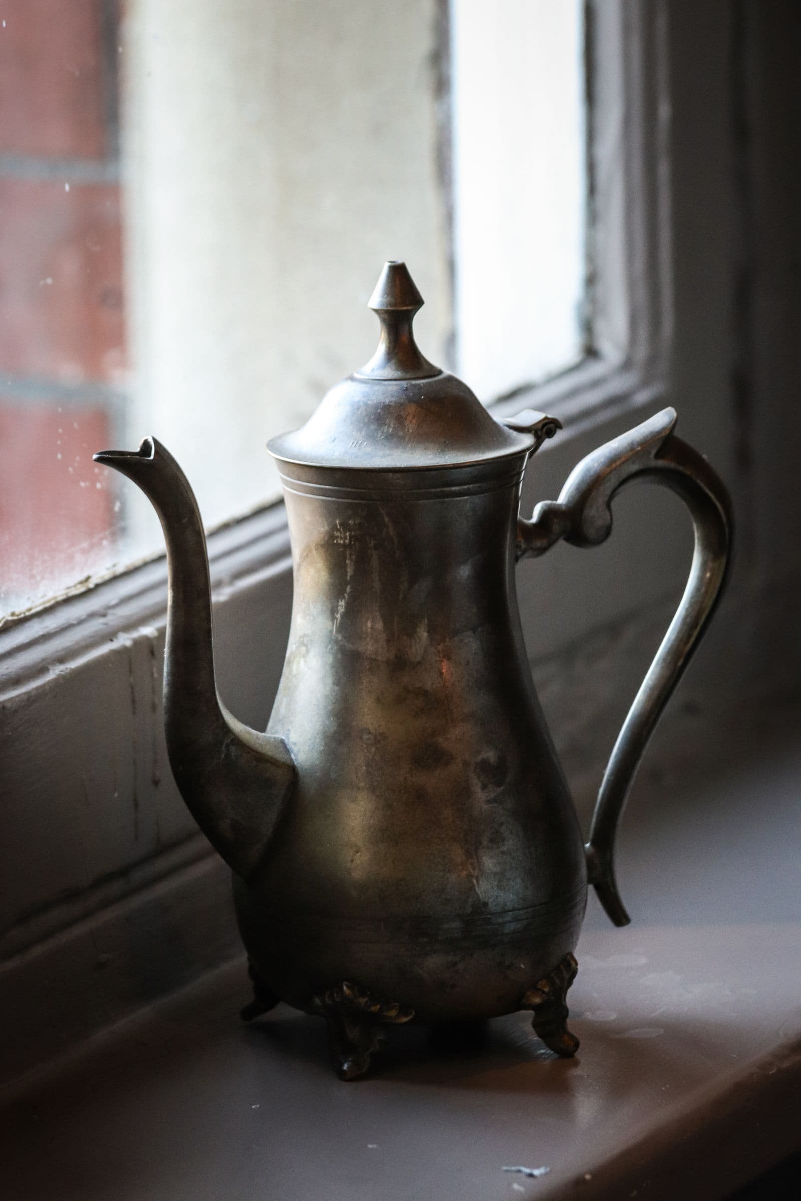An antique metal teapot with heavy patina on a bare windowsill