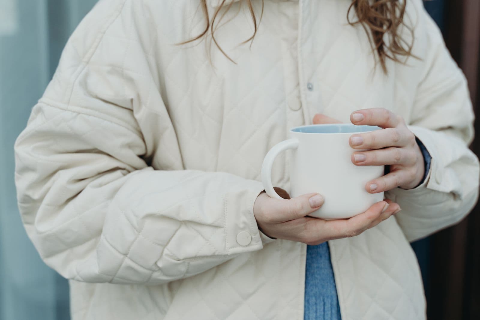 A person in a quilted jacket holding a plain white ceramic mug