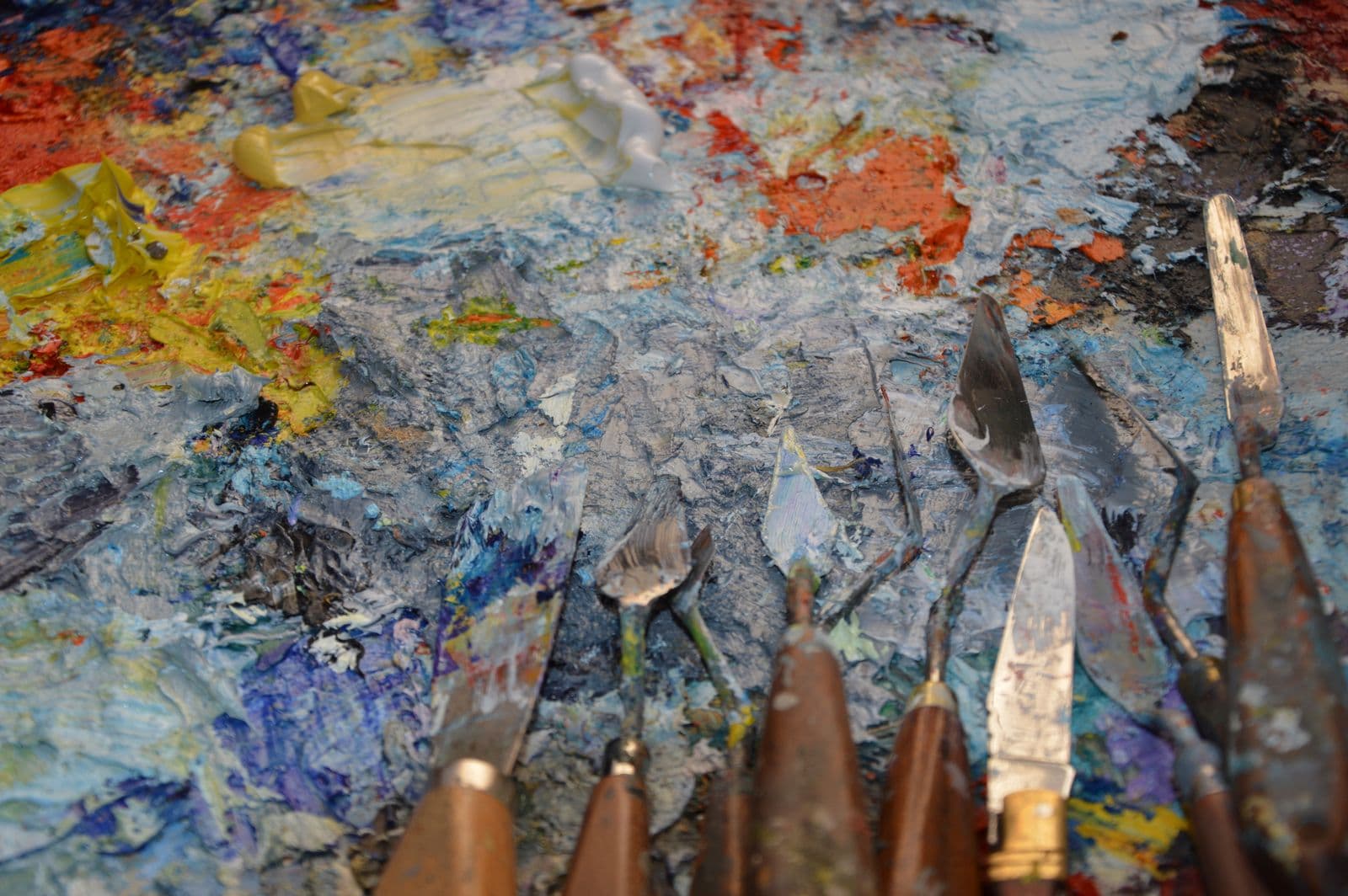 Palette knives resting on a thick oil-paint-crusted palette in the studio