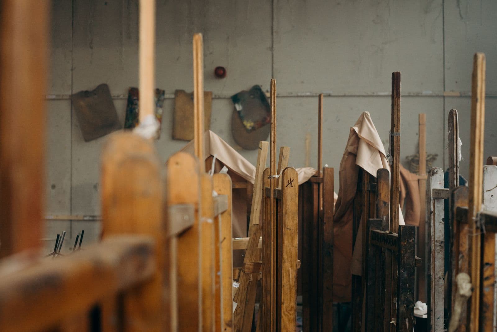 Wooden easels and cloth-draped canvases standing in a muted painting studio.