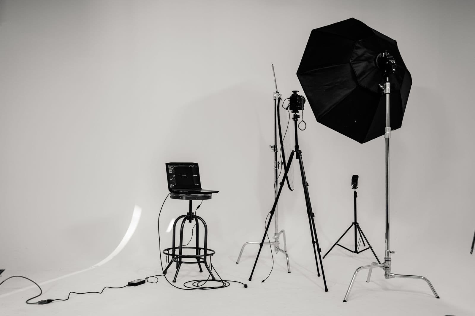 Black-and-white studio set with octabox, tripods, and a tethered laptop on a white cyc