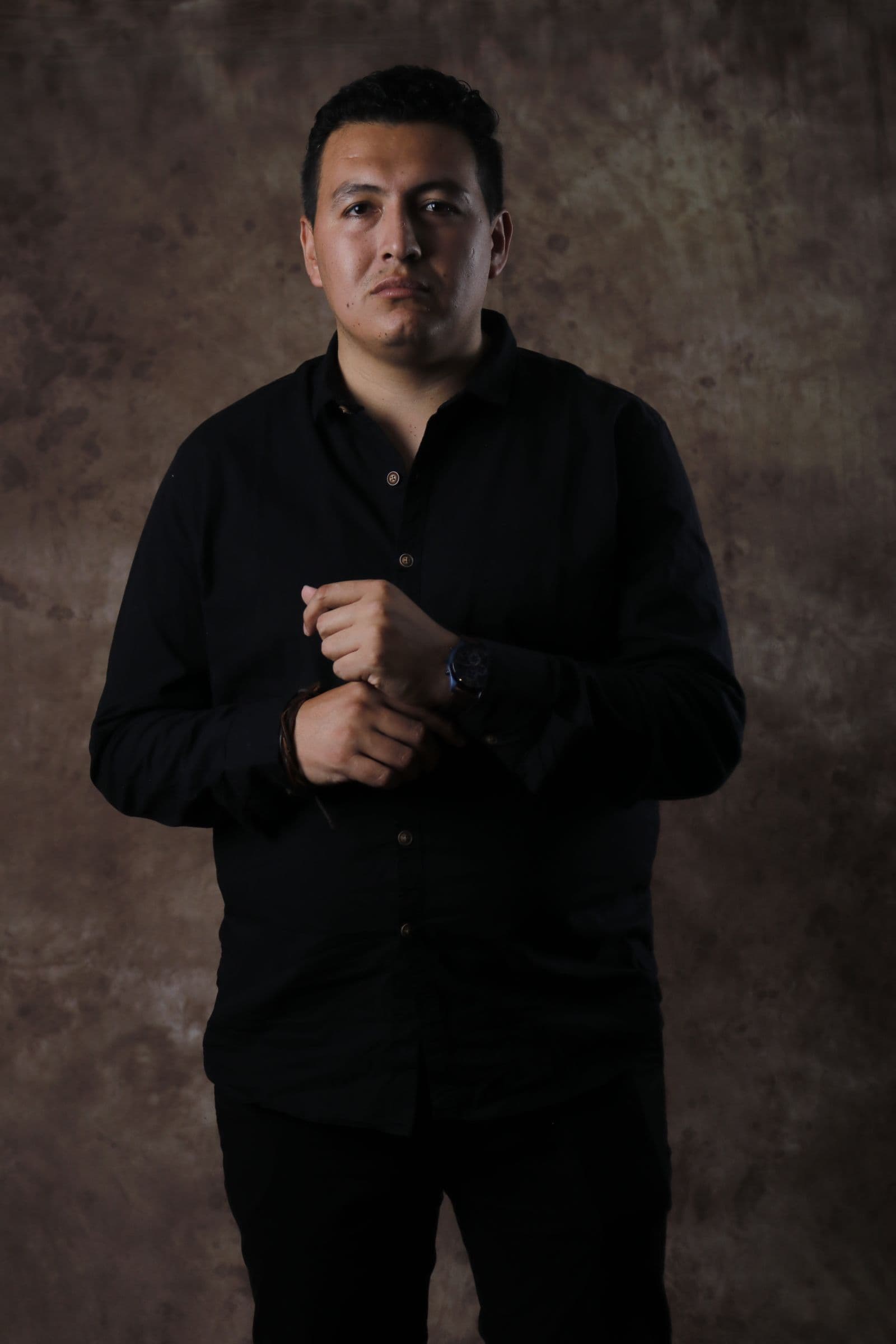 Man in black posed against a hand-painted brown canvas backdrop in dramatic light