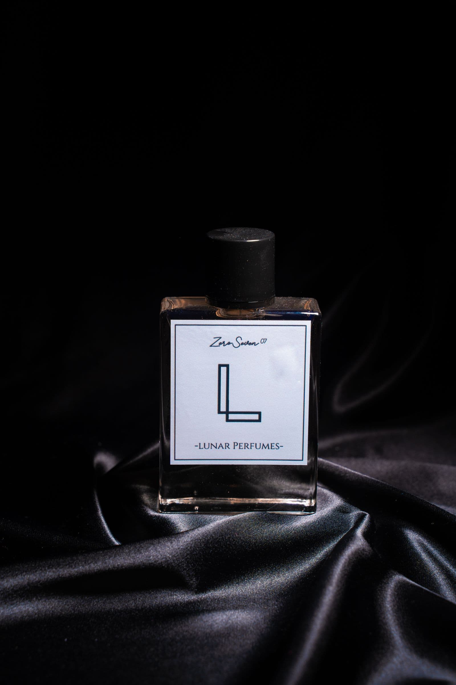 Perfume bottle standing on black silk under a single hard light