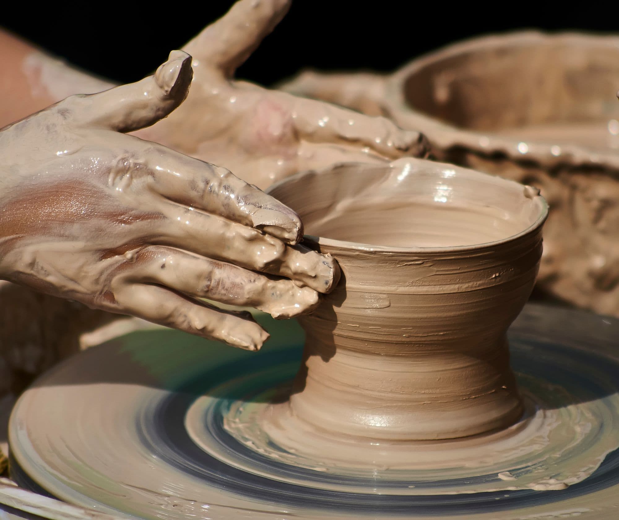 Clay-covered hands shaping the rim of a bowl on a spinning pottery wheel.