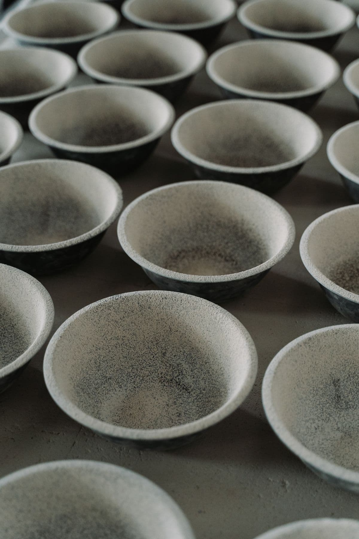 Rows of speckled matte-glaze bowls drying on a table
