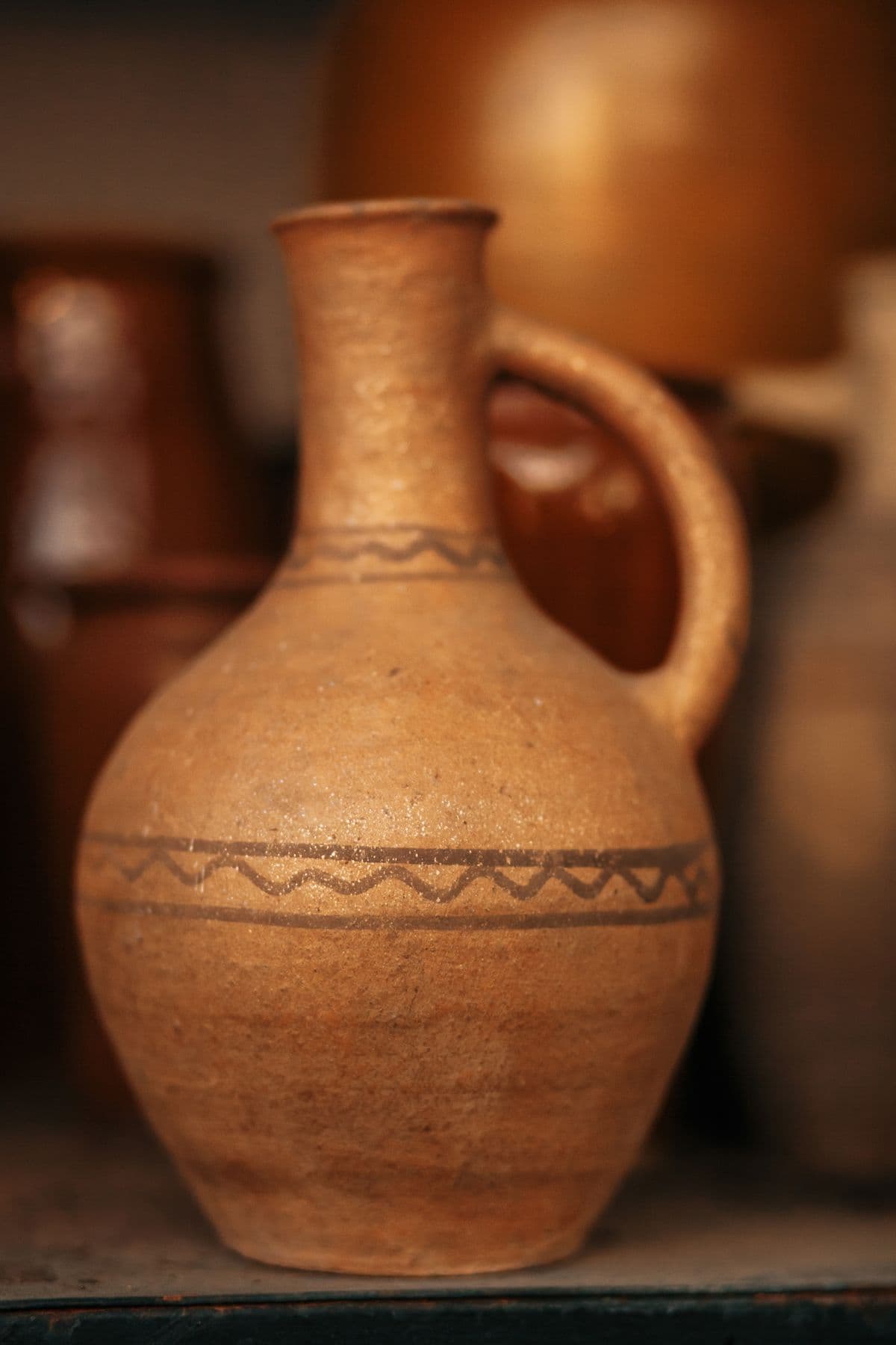 A hand-painted terracotta jug on a shelf of warm pots