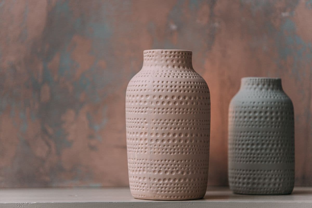 Two dimple-textured vases in blush and sage against a plaster wall